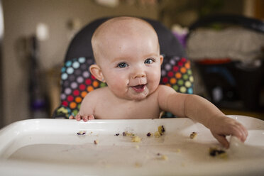 Portrait of shirtless baby girl eating food while sitting on high chair at home - CAVF42344