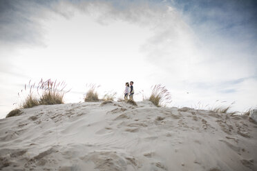 Mittlere Entfernung von Geschwistern auf Sand am Strand gegen bewölkten Himmel stehend - CAVF42347