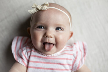 Nahaufnahme eines glücklichen kleinen Mädchens, das seine Zunge herausstreckt, während es sich zu Hause auf dem Bett entspannt - CAVF42354
