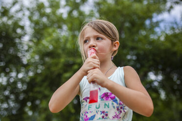 Low angle view of girl looking away while eating flavored ice at park - CAVF42369