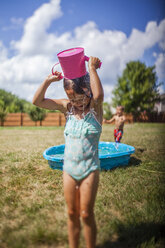 Mädchen gießt Wasser auf den Kopf, während sie auf einer Wiese im Hinterhof steht - CAVF42370