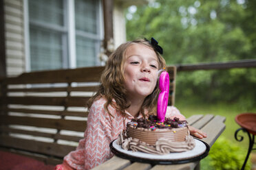 Mädchen bläst Kerze Nummer 6 auf Geburtstagskuchen auf Veranda aus - CAVF42380