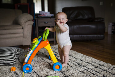Portrait of happy baby girl with walker standing on rug at home - CAVF42381