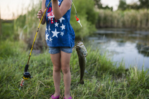 Mittelteil eines Mädchens, das einen gefangenen Fisch in der Angelrute hält, während es am See steht - CAVF42391