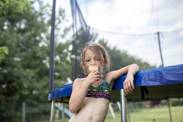 Low angle portrait of girl eating ice cream while standing against trampoline - CAVF42401