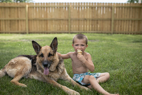 Porträt eines Jungen, der ein Eis isst, während er neben einem deutschen Schäferhund im Hof steht - CAVF42402