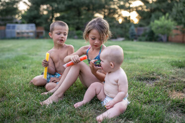Mädchen füttert ihre Schwester mit Eisbonbons, während sie bei ihrem Bruder im Garten sitzt - CAVF42403