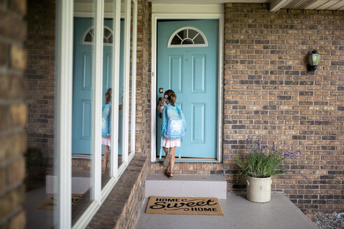 Mädchen mit Rucksack, das die Tür eines Hauses öffnet - CAVF42420