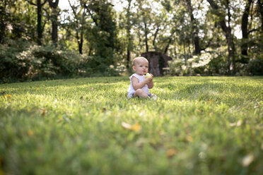 Cute baby girl eating pear while sitting on grassy field - CAVF42430