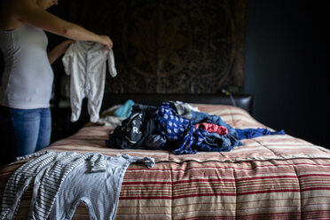 Midsection of woman holding laundry while standing in bedroom - CAVF42447