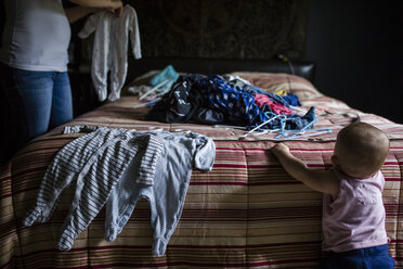 Midsection of mother holding laundry while daughter standing by bed - CAVF42448