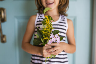 Mittelteil eines Mädchens, das Blumen und Blätter hält, während es vor einer Tür steht - CAVF42454