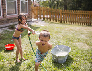 High angle view of playful sister spraying water on shirtless brother through hose at yard - CAVF42460