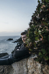 Portrait of hiker sitting on rock by plants against sky - CAVF42484