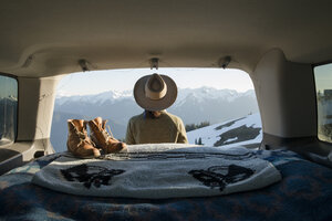 Rear view of female hiker looking at snowcapped mountains while standing outside sports utility vehicle - CAVF42507