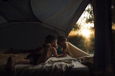 Thoughtful brothers looking through window while lying in tent - CAVF42546