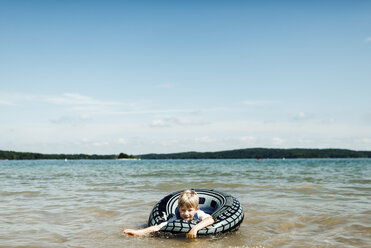 Junge in aufblasbarem Ring spielt im See gegen den Himmel - CAVF42549