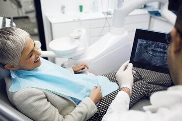 Dentist showing x-ray to happy woman at clinic - CAVF42562