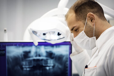 Männlicher Zahnarzt beim Einstellen der Lampe vor dem Röntgenbild in der Klinik - CAVF42571