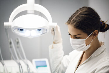 Female dentist adjusting illuminated lamp in clinic - CAVF42583
