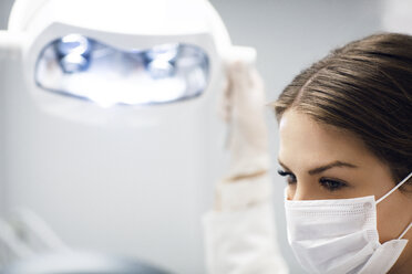 Close-up of female dentist adjusting illuminated lamp in clinic - CAVF42591