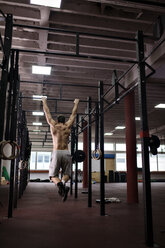 Rückansicht eines Mannes, der Klimmzüge im Fitnessstudio macht - CAVF42597