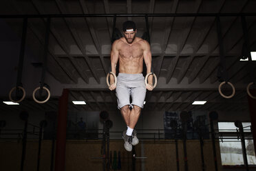 Mann trainiert mit Gymnastikringen in einer Turnhalle - CAVF42598