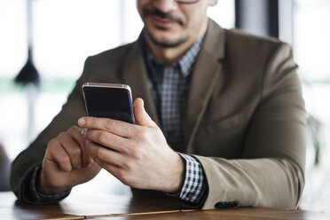 Mittelteil eines lächelnden Geschäftsmannes, der ein Smartphone benutzt und in einem Café sitzt - CAVF42605