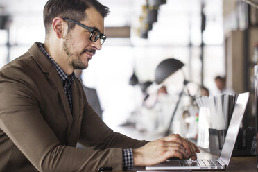 Smiling businessman using laptop while sitting at table in restaurant - CAVF42608