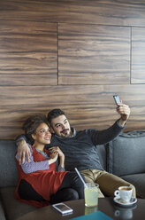 Lächelndes Geschäftspaar, das ein Selfie macht, während es auf dem Sofa im Café sitzt - CAVF42613