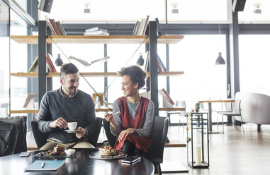 Happy business couple having fruits and coffee while sitting in cafe - CAVF42615