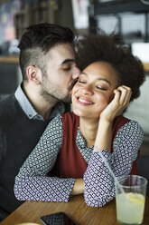 Man kissing happy woman sitting in restaurant - CAVF42621