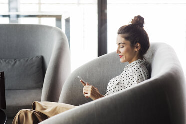 Side view of businesswoman using phone while sitting on sofa at restaurant - CAVF42633