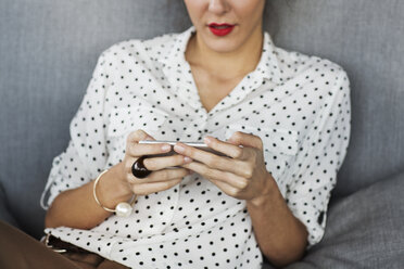 Mittelteil einer Geschäftsfrau, die ihr Smartphone auf dem Sofa im Restaurant benutzt - CAVF42634