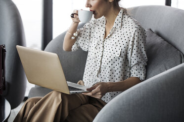 Frau trinkt Kaffee, während sie im Restaurant am Laptop arbeitet - CAVF42635