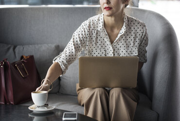 Geschäftsfrau hält Kaffeetasse, während sie im Restaurant am Laptop arbeitet - CAVF42636