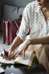 Businesswoman writing in diary at table in restaurant - CAVF42638