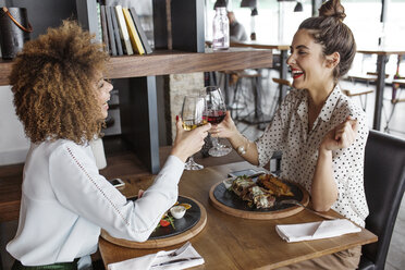 Glückliche Geschäftsfrauen stoßen mit Weingläsern am Tisch im Restaurant an - CAVF42643