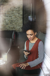 Geschäftsfrau, die ein Smartphone benutzt, während sie auf dem Sofa im Café sitzt - CAVF42659