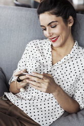 Happy businesswoman using smart phone while sitting on sofa at restaurant - CAVF42669