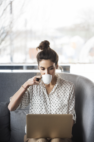 Geschäftsfrau trinkt Kaffee, während sie im Restaurant am Laptop arbeitet, lizenzfreies Stockfoto