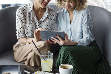 Midsection of female colleagues using tablet computer while sitting on sofa at cafe - CAVF42678