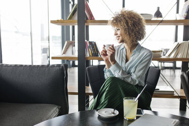 Nachdenkliche Geschäftsfrau lächelt und hält ihr Smartphone in einem Café - CAVF42688