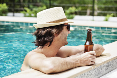 Side view of man holding beer bottle in swimming pool - CAVF42693