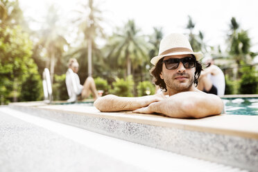 Thoughtful man relaxing in swimming pool with friends in background - CAVF42714