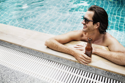High angle view of man holding beer bottle in swimming pool - CAVF42718