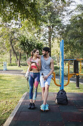 Front view of happy couple leaning over exercise equipment at park - CAVF42740