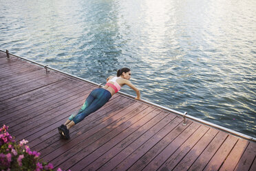 High angle view of woman performing pushups at wooden walkway by river - CAVF42749
