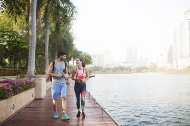 Couple smiling and walking on wooden walkway at riverbank - CAVF42751