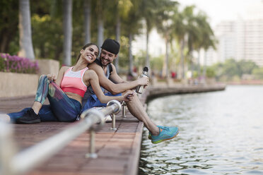 Happy couple sitting and enjoying on wooden walkway at riverbank - CAVF42752